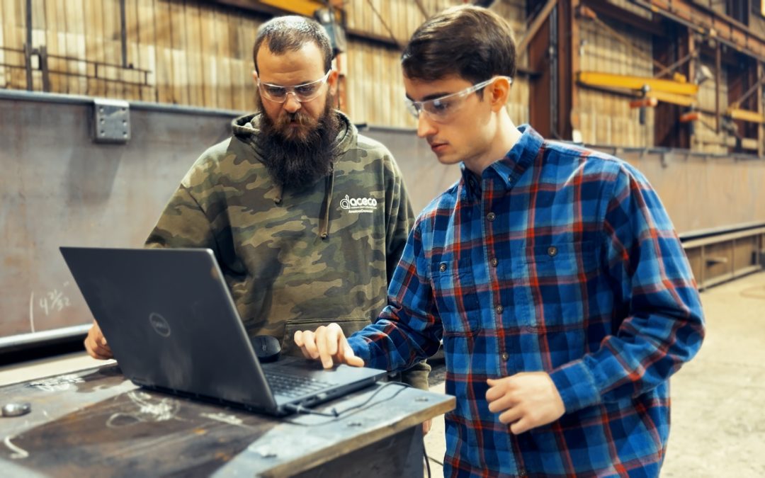 Two men working on a computer in a manufacturing shop